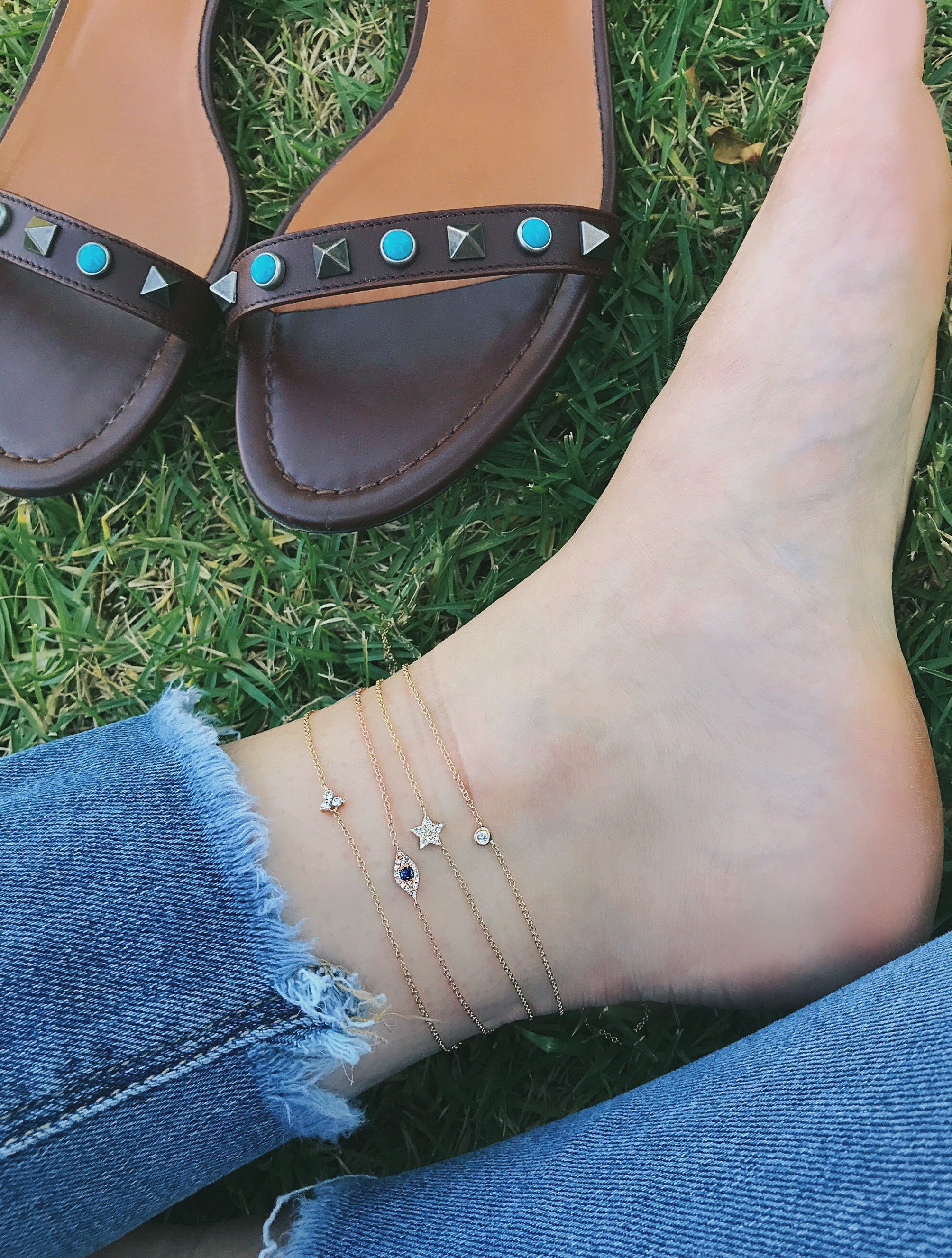 Diamond Evil Eye Anklet in 14k yellow gold styled on ankle of model with tree additional anklets