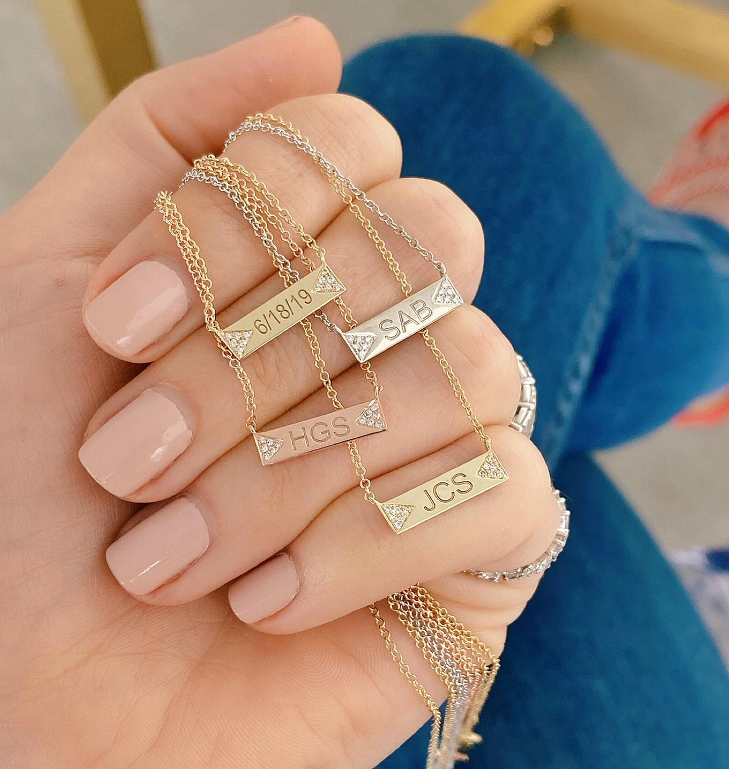 Diamond Double Triangle Mini Nameplate Necklaces held in hand of model featuring 14k rose gold yellow gold and white gold