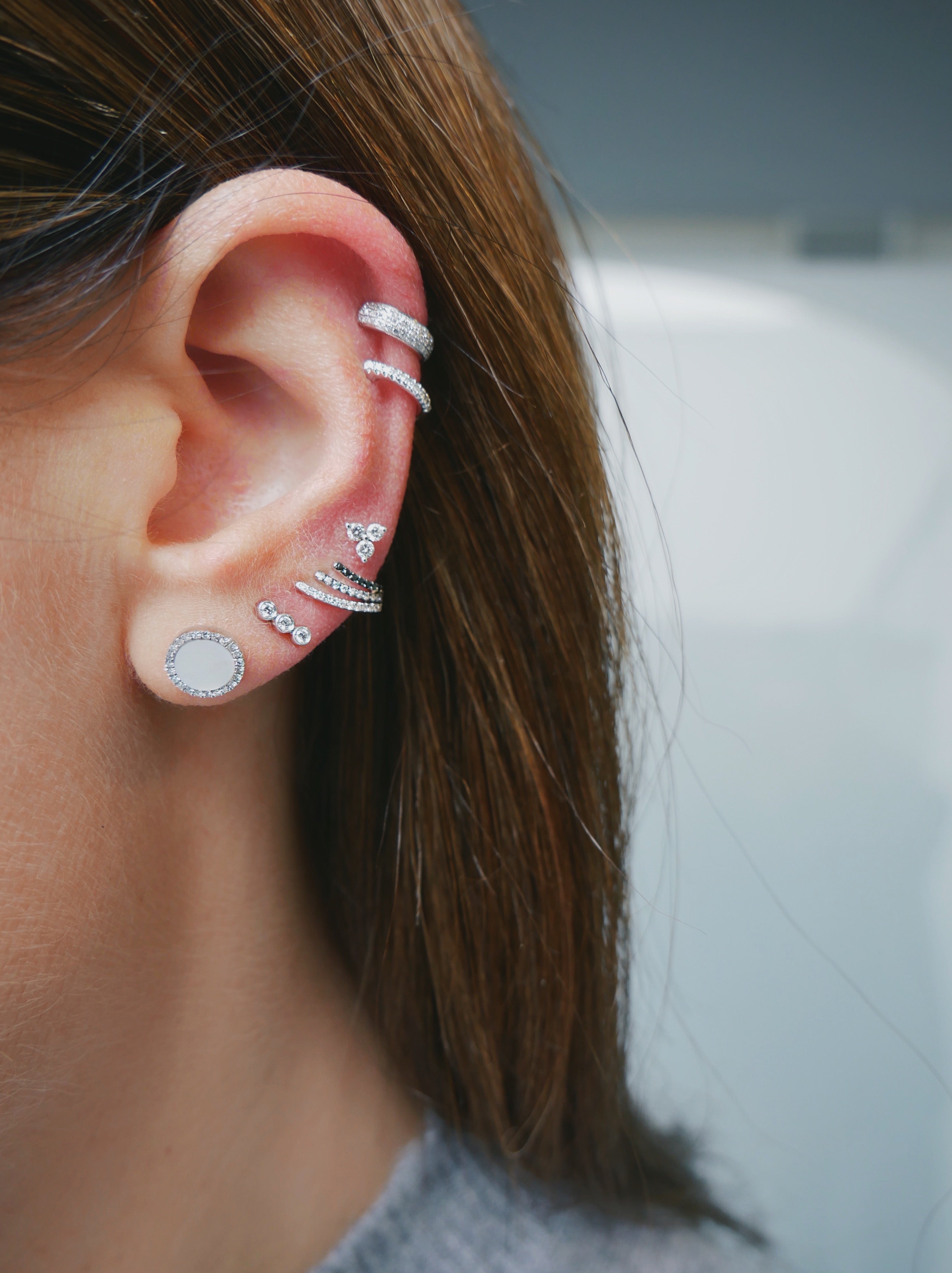 Diamond Triple Bezel Stud Earring in 14k white gold styled on ear of model with five additional earrings styled