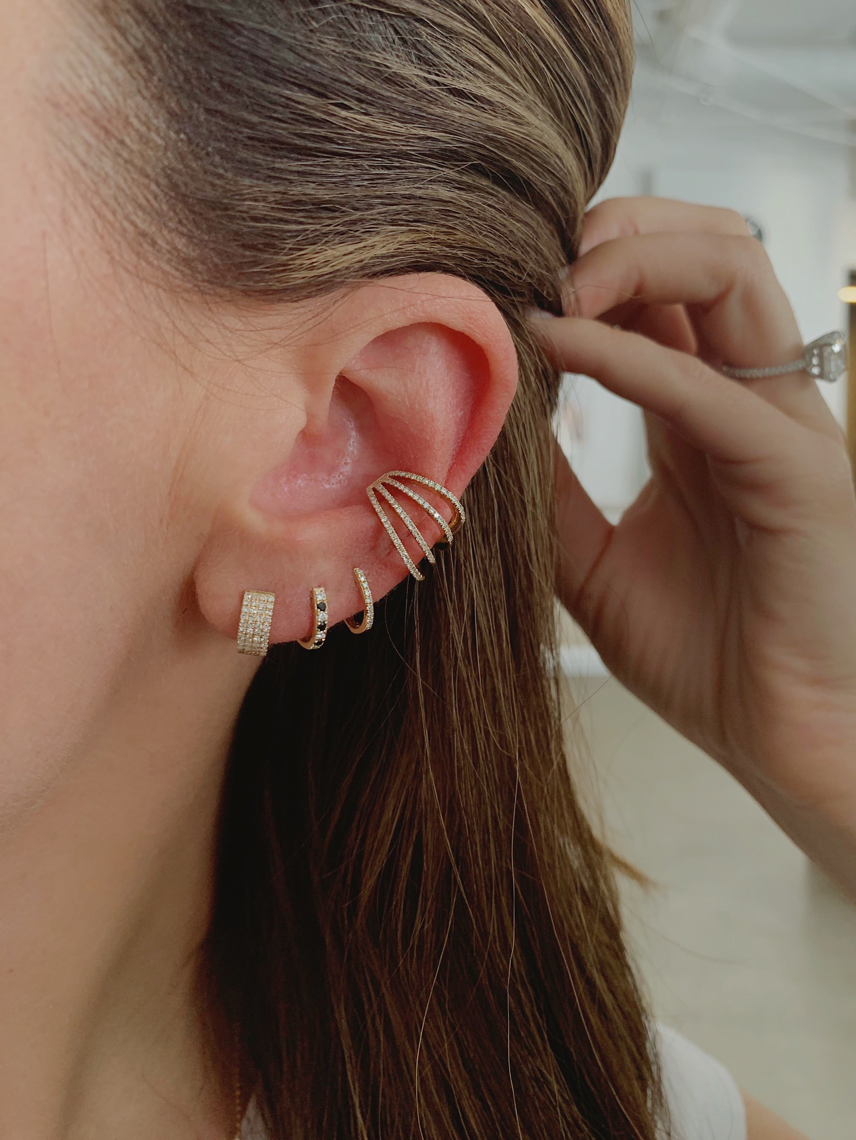 Mini Diamond & Black Diamond Dot Huggie Earring in 14k yellow gold styled on second earring hole of earlobe of model with three additional earrings styled