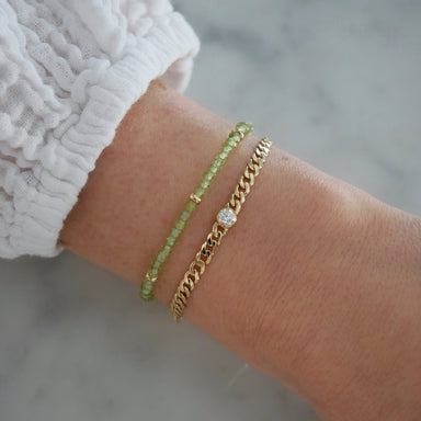 Diamond Sari Bracelet in 14k yellow gold styled on wrist of model next to green beaded bracelet