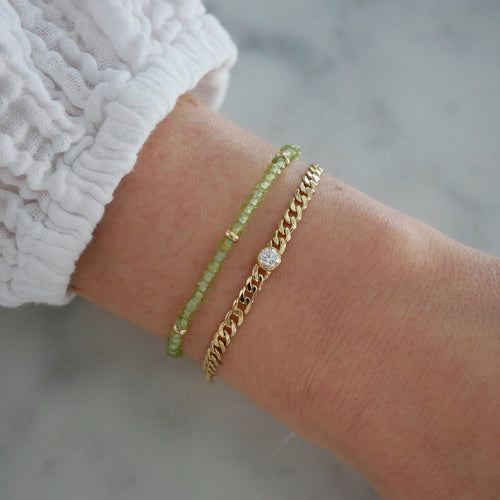 Diamond Sari Bracelet in 14k yellow gold styled on wrist of model next to green beaded bracelet