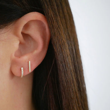 Gold Mini Bar Stud Earring in 14k yellow gold styled on ear lobe of model next to diamond baguette huggie earring