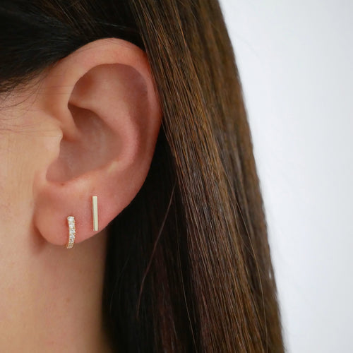Gold Mini Bar Stud Earring in 14k yellow gold styled on ear lobe of model next to diamond baguette huggie earring