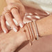 Endless Love Eternity Bracelet in 14k rose gold styled on wrist of model with diamond bracelets and rose gold rings styled on fingers of model