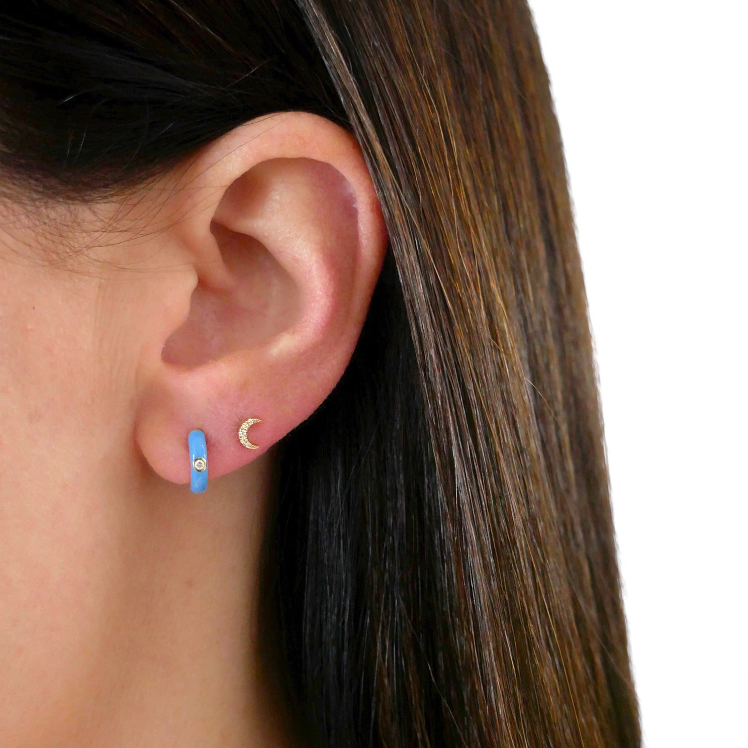 Diamond Blue Enamel Huggie Earring in 14k yellow gold styled on ear lobe of ear next to mini moon stud earring on ear of model