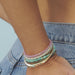 Birthstone Bead Bracelet in Turquoise styled on wrist with layered birthstone bead bracelets, gold treasure bangle and gold layered rings styled on fingers of model putting thumb in back pocket of jeans with no audio