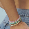 Birthstone Bead Bracelet in Turquoise styled on wrist with layered birthstone bead bracelets, gold treasure bangle and gold layered rings styled on fingers of model putting thumb in back pocket of jeans with no audio