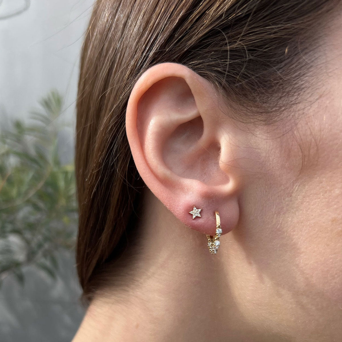 Diamond Star Stud Earring in 14k yellow gold styled on second earring hole on earlobe of model with bezel teardrop huggie earring on first earring hole
