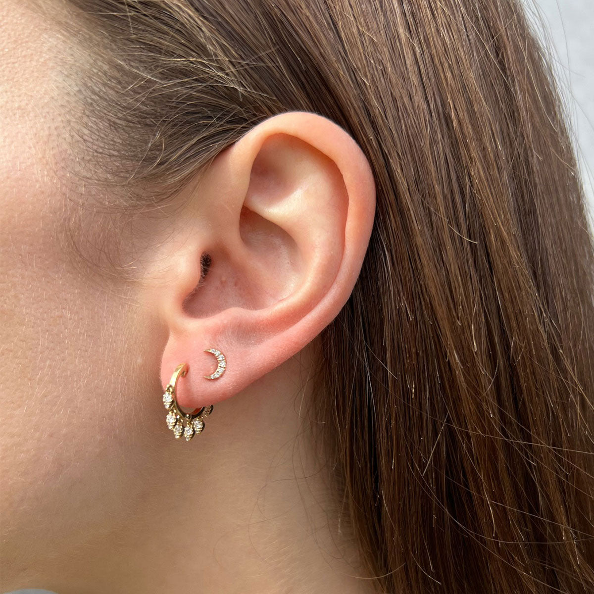 Diamond Mini Moon Stud Earring in 14k yellow gold styled on second earring hole on ear lobe of model with brown hair