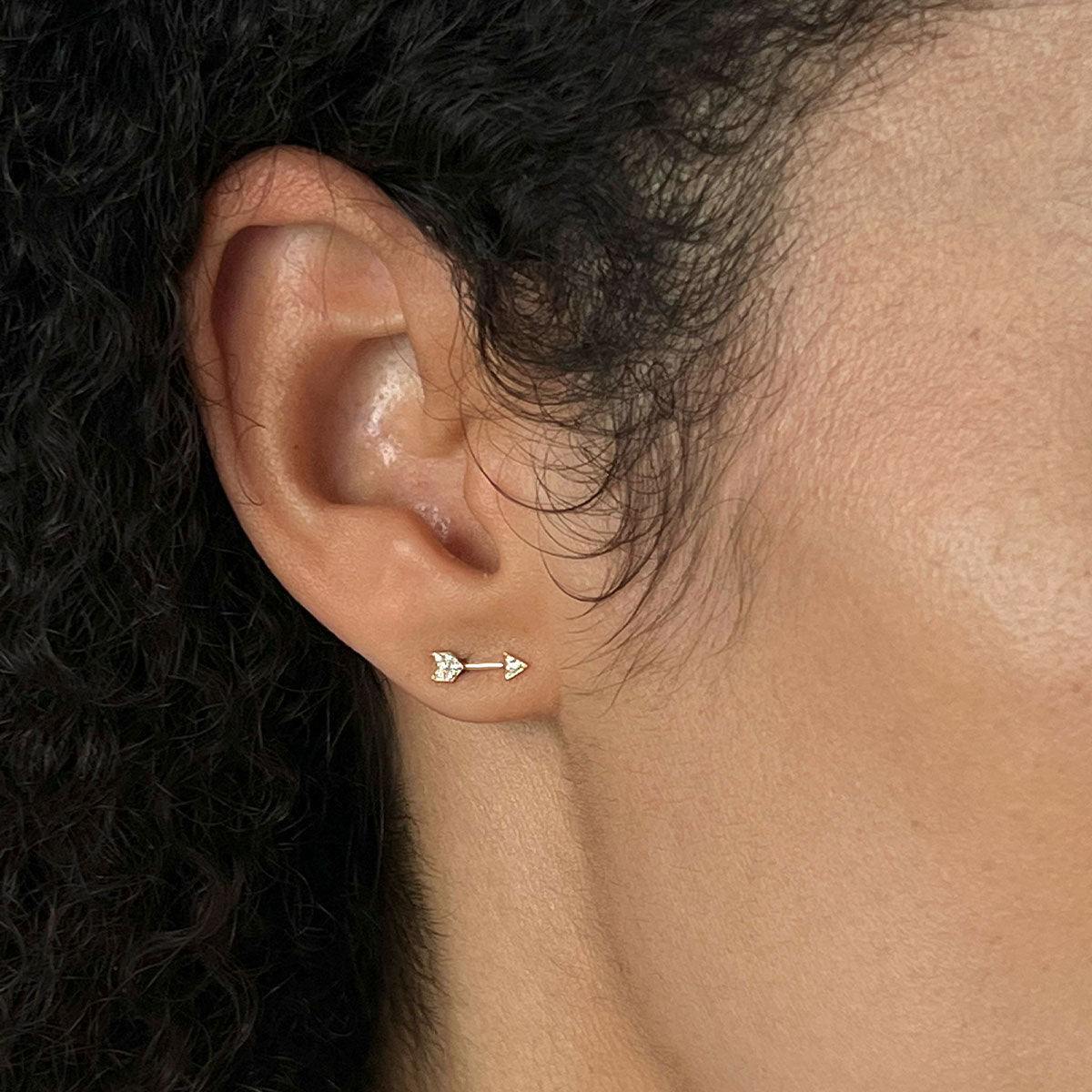 Diamond Mini Arrow Stud Earring in 14k yellow gold styled on earlobe of model with brown hair